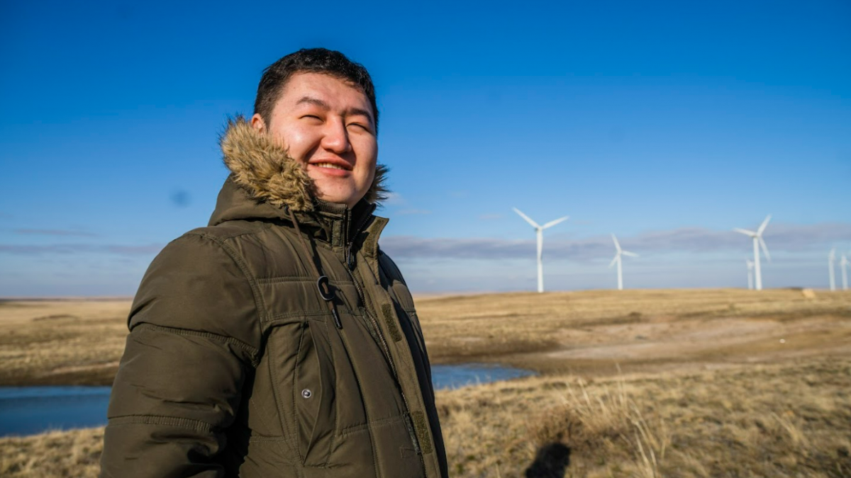 A man poses in a field in front of windmills.