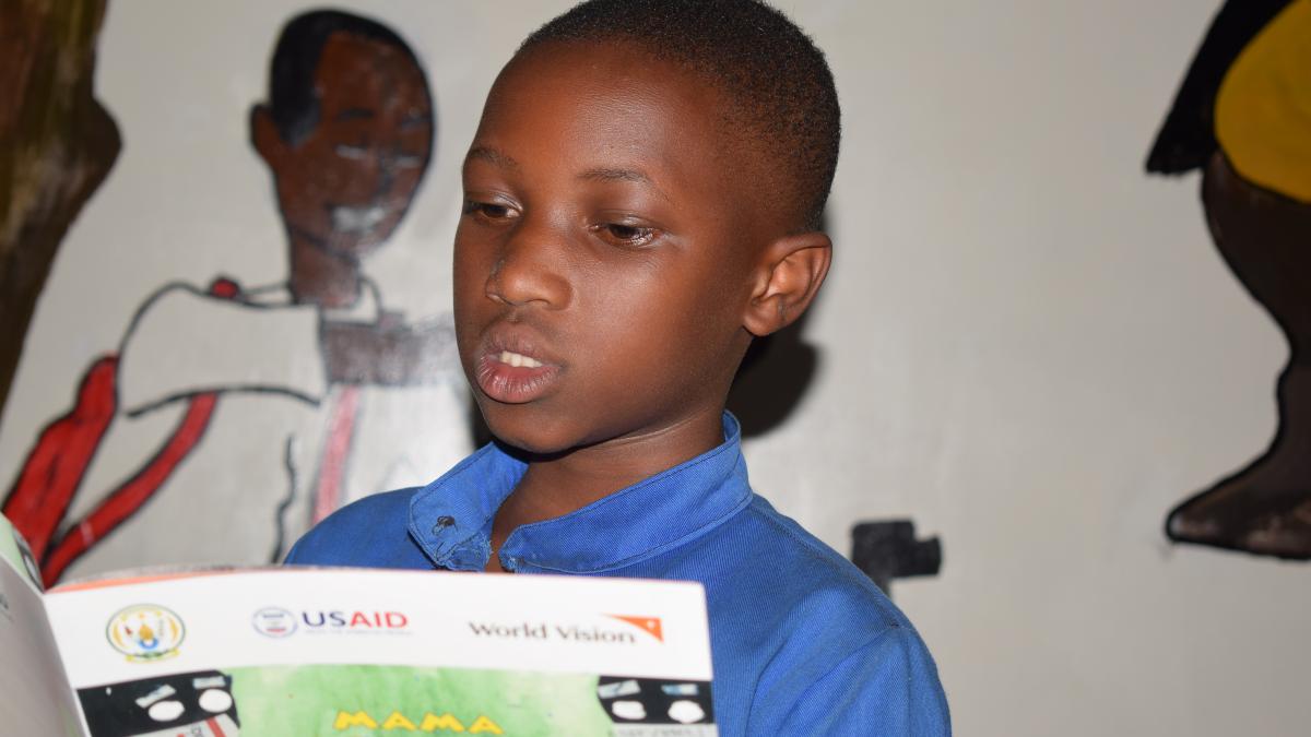 Sarah reading a book printed with the support of USAID.